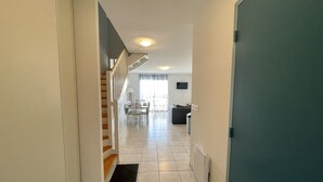 Corredor que leva a uma sala de jantar, com escadas, um sofá e uma TV.