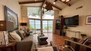 Un salón amplio con un gran ventanal que ofrece vistas al mar, un televisor de pantalla plana montado en la pared y una zona de estar acogedora con sofá y sillones.