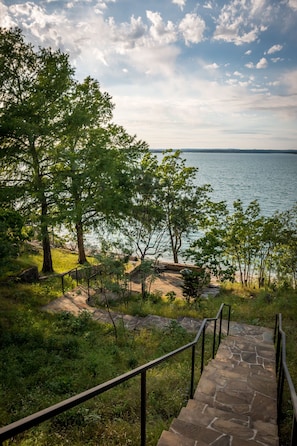 Stroll down the stone staircase to a tranquil grassy area surrounded by lush greenery and trees.