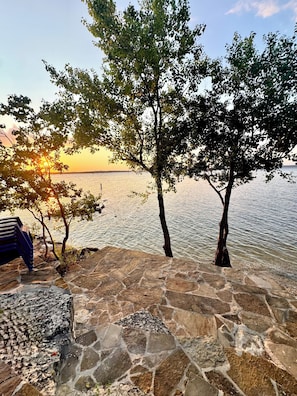 A stone patio with a view of a calm body of water and trees.