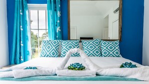 A neatly made bed with white and blue patterned pillows, a large mirror above it, and blue curtains. - Summers Dream....  your dreams become a reality. (Negril)