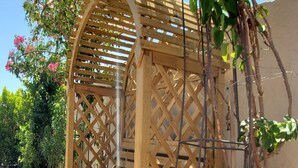 Une structure de jardin en bois, ornée d’un motif en treillis, entourée de rochers et de plantes en pot.