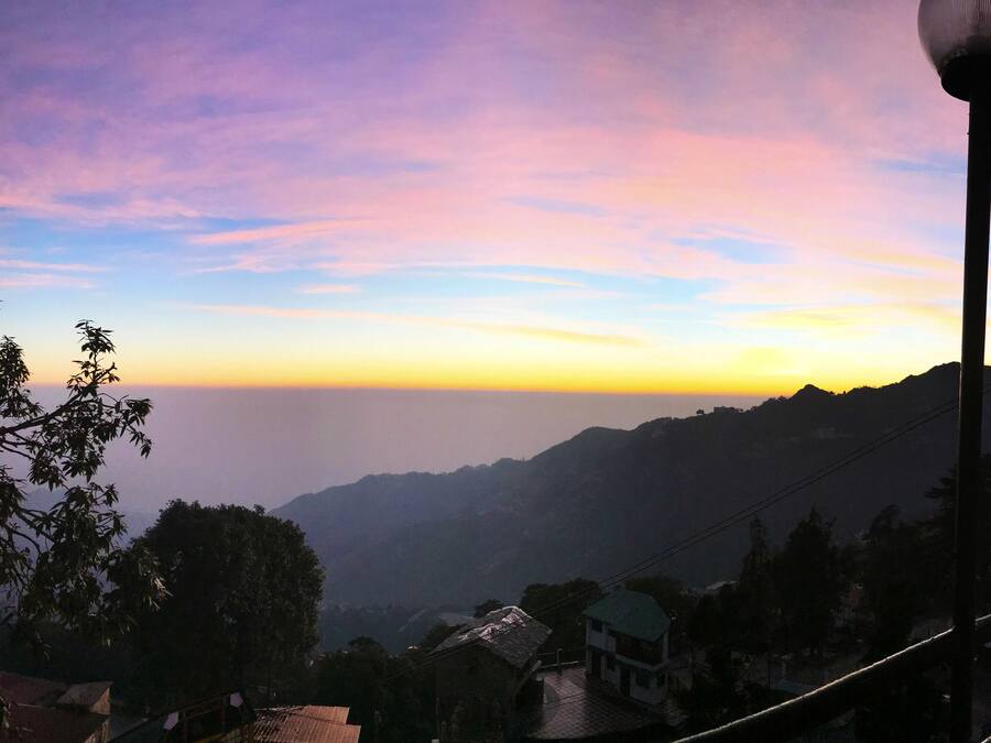 A hotel with a checkered terrace, a view of the mountains, and a sunset sky.
