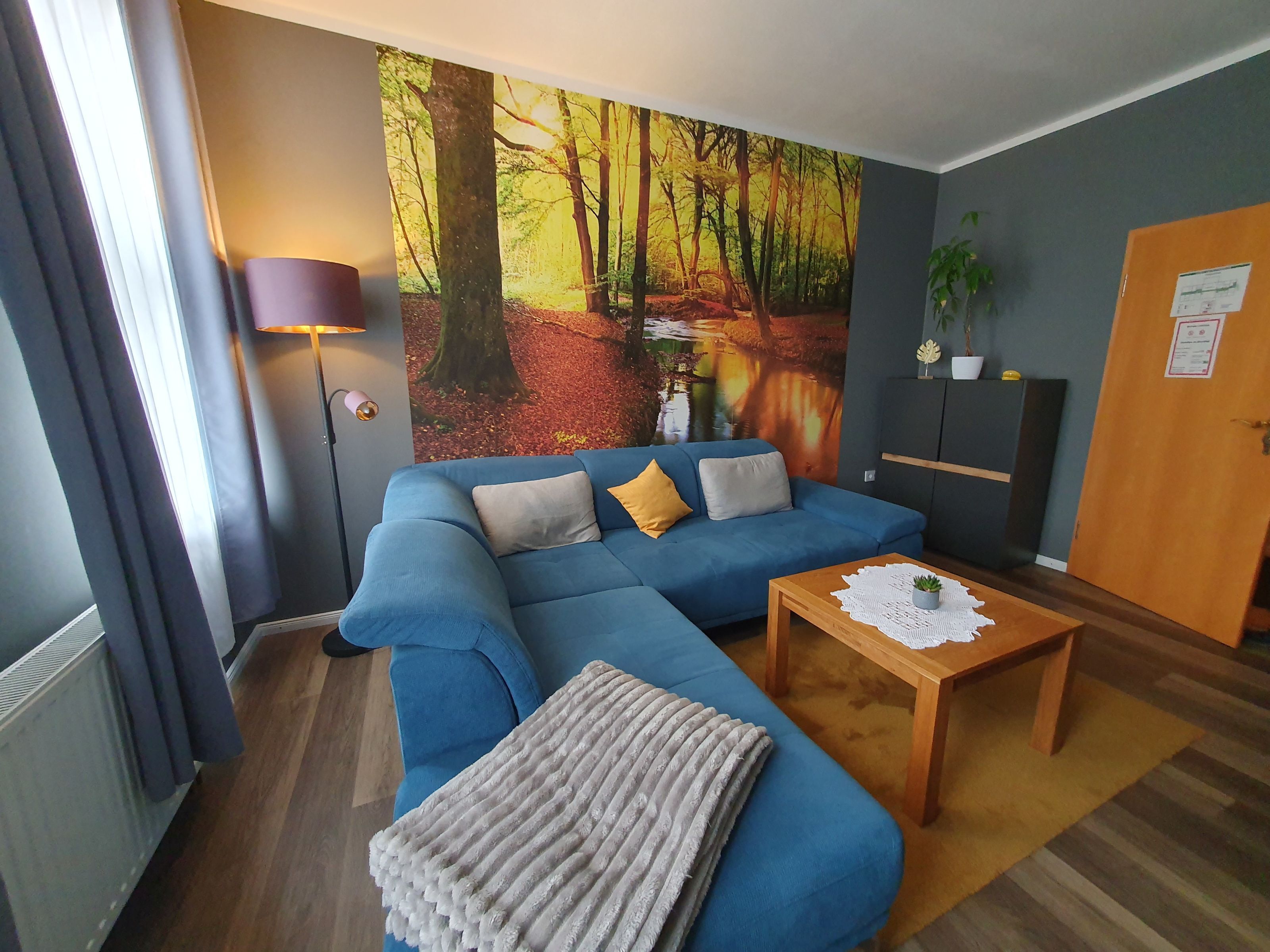 Un salón con un sofá azul, una mesa de centro de madera y un mural temático de bosque.