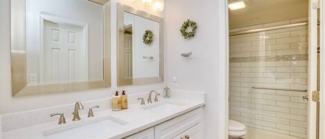 Une salle de bain avec un meuble-lavabo blanc, deux vasques, un grand miroir et un espace douche doté d’une porte en verre.