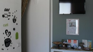 Una habitación con pared blanca, un televisor montado, una consola con cajones y decoraciones en la pared que incluyen ilustraciones de tazas de café y la palabra 'CAFE'.