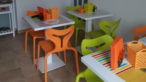 Un comedor con sillas y mesas coloridas, una puerta blanca y una pared con cuadros.