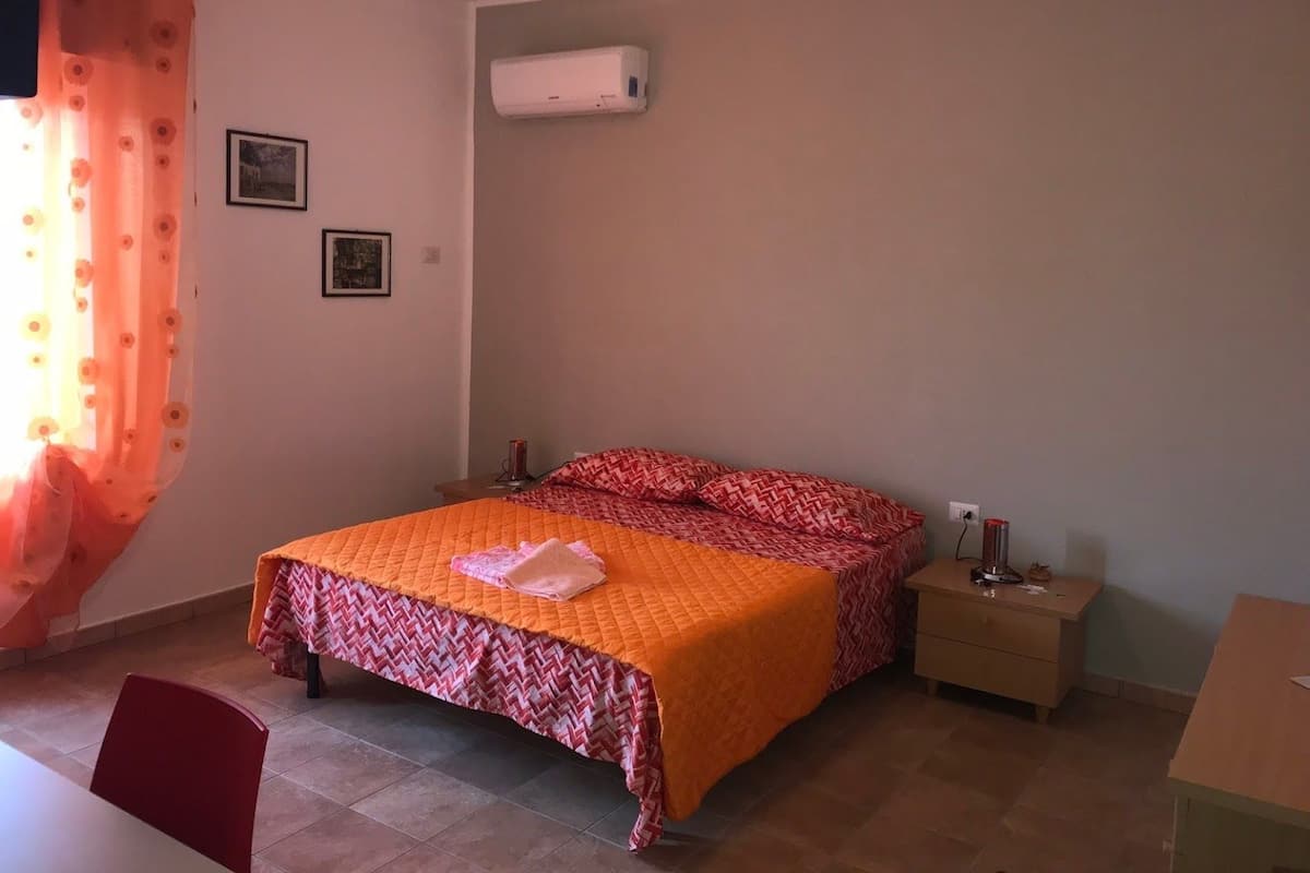 A bedroom with a bed, bedside tables, an air conditioner, and a window with curtains.