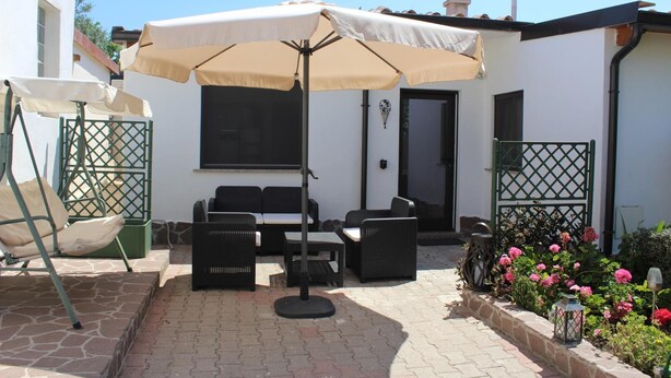 Un área de patio al aire libre con una mesa, sillas y una mecedora, además de un paraguas grande.