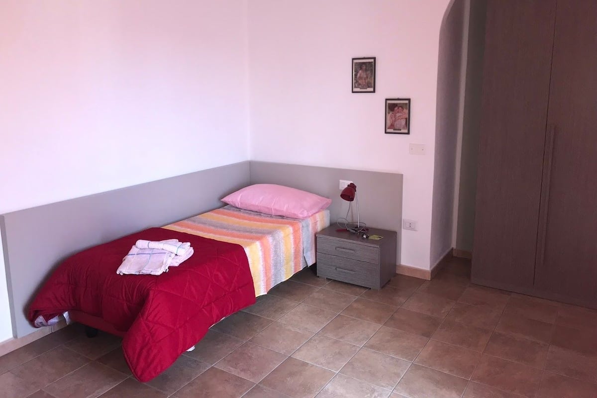 A small bedroom with a single bed, a nightstand, a red lamp, and a wardrobe.