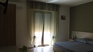 Un dormitorio con cama, una silla, una mesa y una ventana con cortinas.