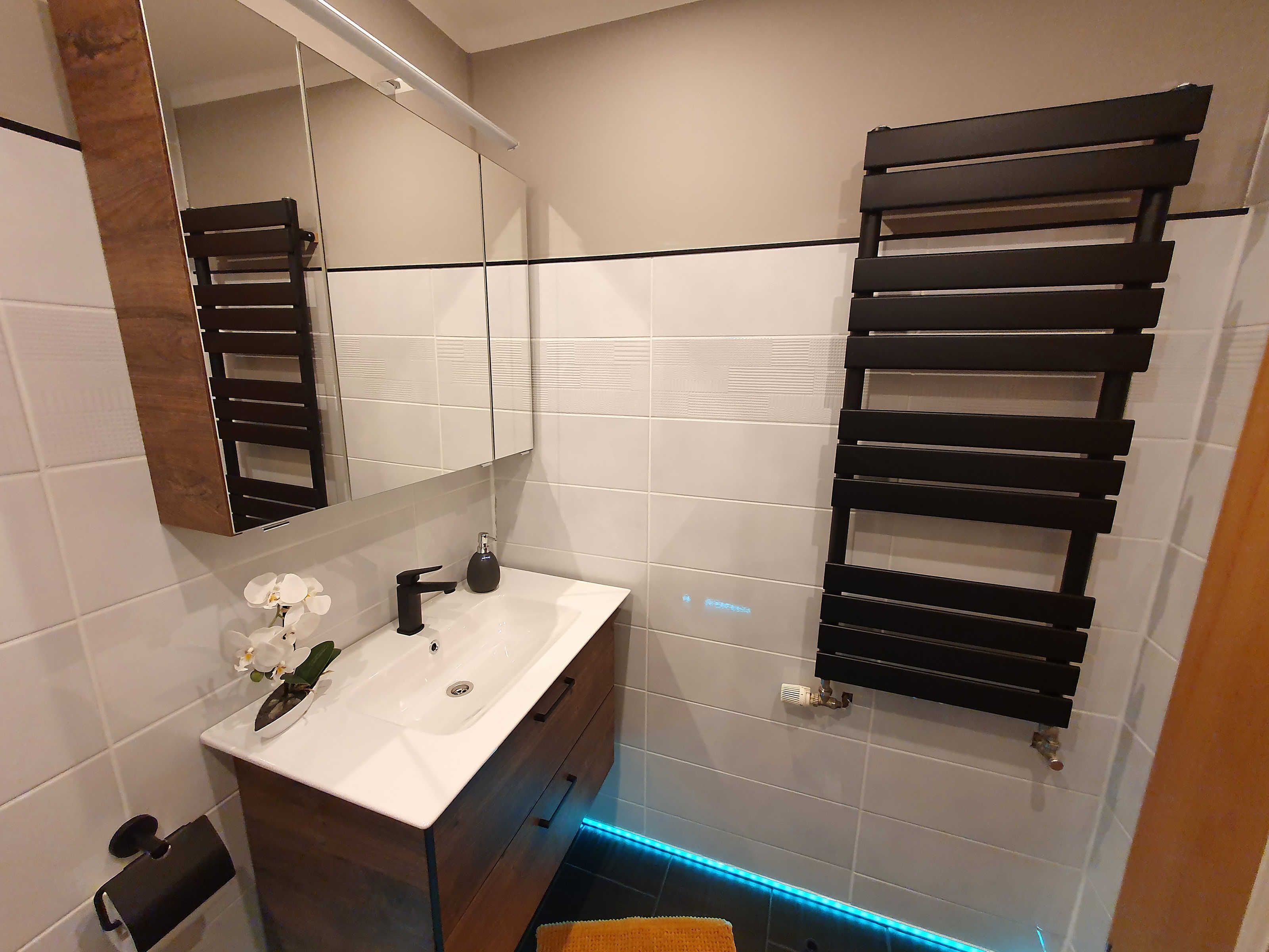 A modern bathroom with a white sink, dark wooden vanity, a mirror, and a towel rack.