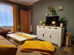 Un salon avec un canapé, une table basse, un téléviseur posé sur un meuble et une plante en pot.