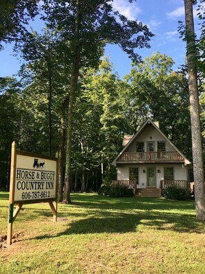 A wooden house with a porch, surrounded by trees, and a sign for Horse & Buggy Country Inn. - The Horse & Buggy Country Inn (Liberty)