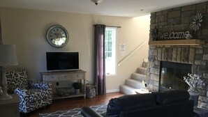 Una sala de estar con chimenea, un reloj, un televisor y un sofá.