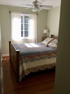 A bedroom with a wooden bed, a ceiling fan, a window with curtains, and a bedside lamp. - The Horse & Buggy Country Inn (Liberty)