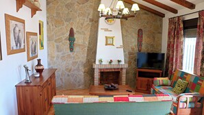 A cozy living room with a stone wall, a fireplace, a television, and a colorful sofa. - Holiday home with fenced private pool (CONIL DE LA FRONTERA)