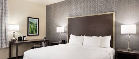 A hotel room with a large bed, two bedside tables with lamps, a desk, a chair, and a framed picture on the wall.