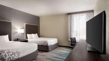 A hotel room with two beds, a desk, a flat-screen TV, and a large window with curtains.