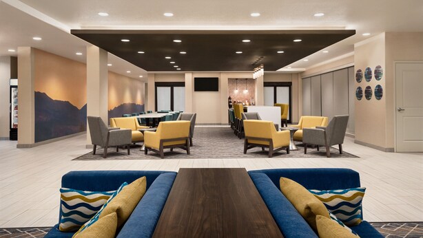 A hotel lobby with a central seating area, a dining section, and a reception desk.