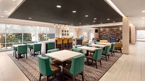 A modern dining area with multiple tables and chairs, large windows, and a patterned floor.