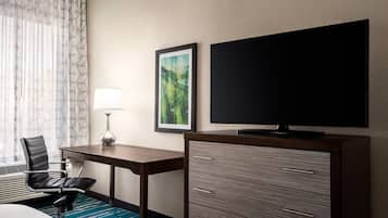 A hotel room with a desk, chair, TV, and a cabinet.