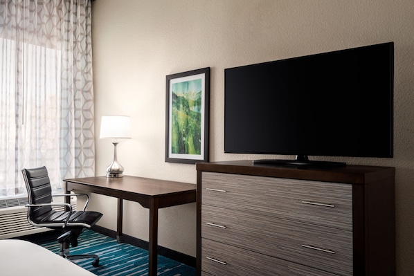 A hotel room with a desk, chair, TV, and a cabinet.