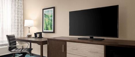 A hotel room with a desk, chair, television, and a framed picture on the wall.