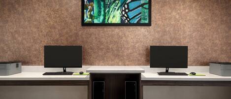 A reception desk with two monitors, a framed artwork above, and a wooden cabinet below.
