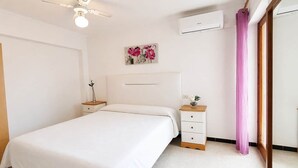 Une chambre à coucher comprenant un lit, des tables de chevet, un ventilateur de plafond, un appareil de climatisation et une fenêtre avec un rideau.