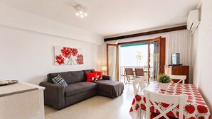 Un salon comprenant un canapé, une table à manger avec des chaises, un téléviseur et une fenêtre avec des rideaux.