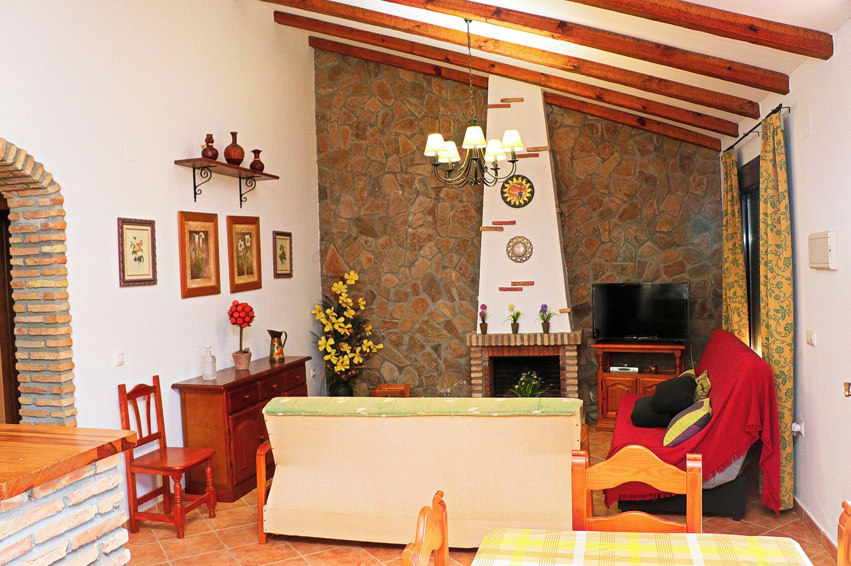 A cozy living room with a stone fireplace, wooden beams, a television, and a dining area with a table and chairs.