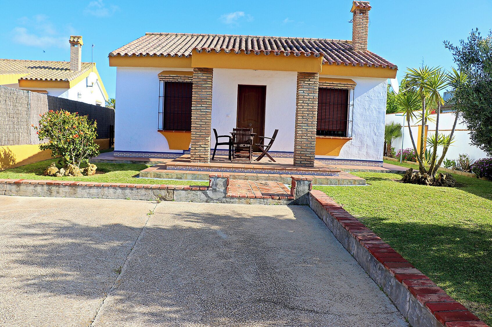 Une maison à deux étages, avec un toit recouvert de tuiles, un porche à l’avant doté d’un banc et un petit jardin.