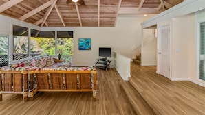 A spacious room with a high ceiling, wooden flooring, a large bed with a floral bedspread, a television, and a staircase leading to another level. - Peaceful Location with Lush Tropical Views (Princeville)