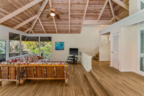 A spacious room with a high ceiling, wooden flooring, a large bed with a floral bedspread, a television, and a staircase leading to another level.