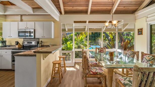 A spacious kitchen with white cabinets, a wooden ceiling, and a large island with stools. - Peaceful Location with Lush Tropical Views (Princeville)