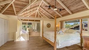 A spacious bedroom with a four-poster bed, wooden ceiling beams, and a large window offering a view of the outdoors. - Peaceful Location with Lush Tropical Views (Princeville)