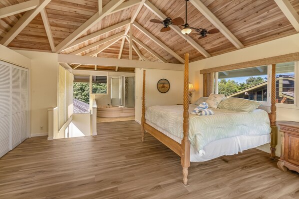 A spacious bedroom with a four-poster bed, wooden ceiling beams, and a large window offering a view of the outdoors.