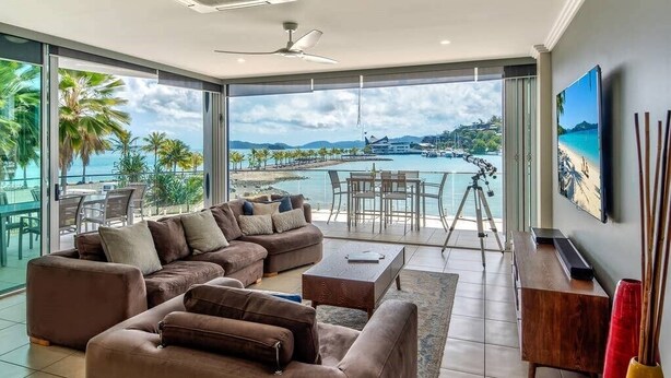 Ein modernes Wohnzimmer mit einer großen Couch, einem Couchtisch und einem Essbereich mit Blick auf Strand und Wasser.