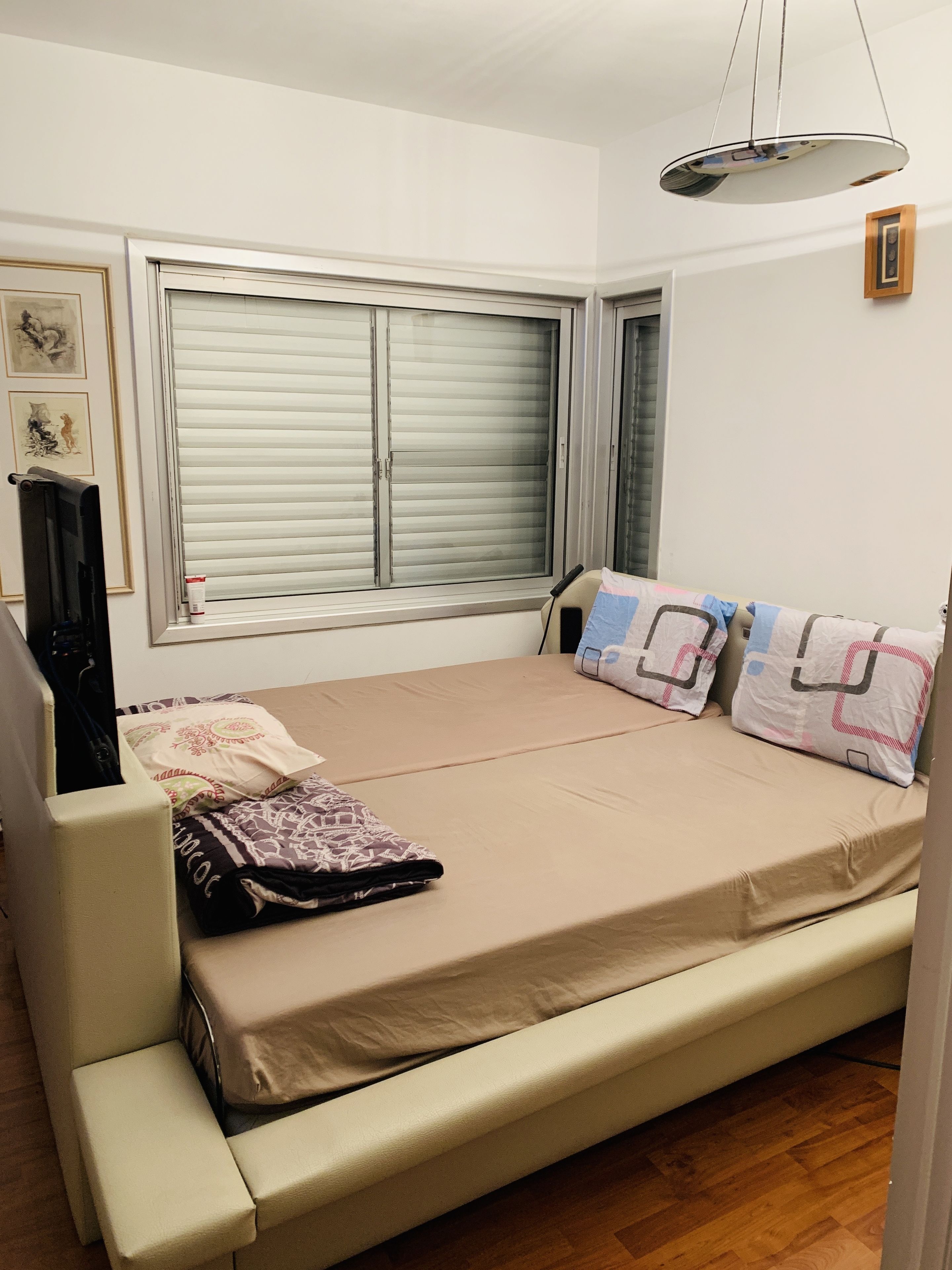 A small, neatly arranged bedroom with a bed, a chair, a window with blinds, and a ceiling light.