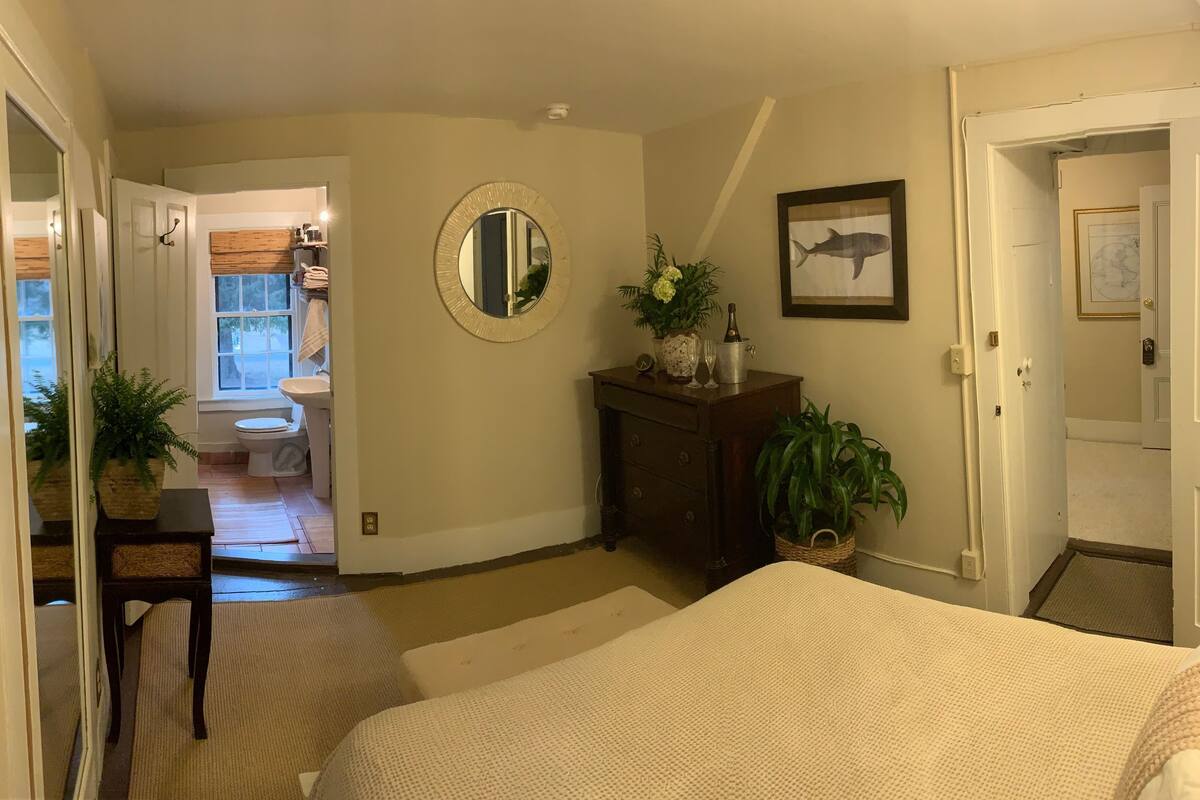 A bedroom with a bed, a dresser, a mirror, and a door leading to a bathroom.