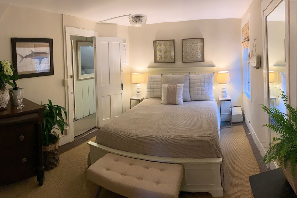 A bedroom with a bed, bedside tables, a bench, a dresser, and decorative items.