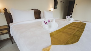 Una cama cuidadosamente arreglada con sábanas blancas, una manta marrón y dos toallas con forma de cisne decoradas con flores moradas.