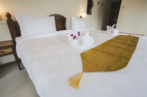 A neatly made bed with white linens, a brown throw blanket, and two swan-shaped towels with purple flowers.
