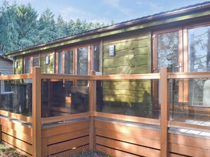 Une cabane en bois dotée de grandes fenêtres, d’une terrasse en bois et d’un mur en pierre.