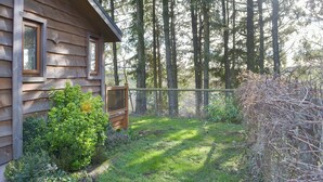 Eine Holzhütte mit eingezäuntem Hof, umgeben von hohen Bäumen.