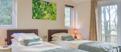 Habitación doble con dos camas, una mesita de noche con lámpara, un enchufe y una ventana con cortinas.