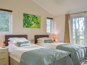 Une chambre double avec deux lits, une table de chevet avec une lampe, une prise de courant et une fenêtre avec des rideaux.
