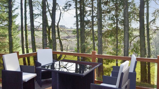 Ein überdachter Außenbereich mit Korbmöbeln und einem Glastisch, mit Blick auf eine bewaldete Landschaft.