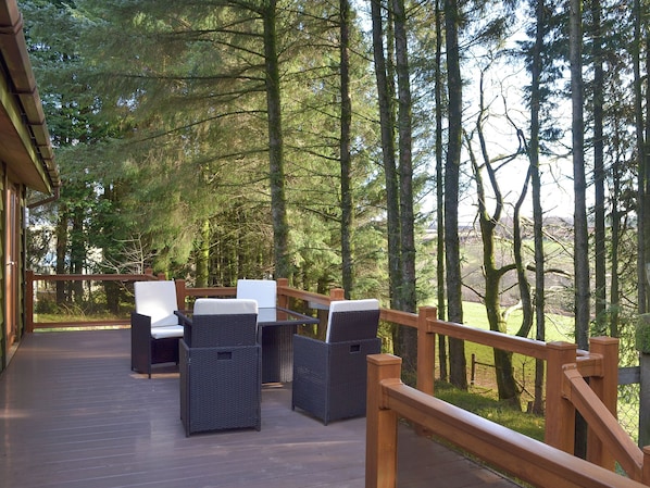 A wooden deck with wicker furniture and a view of a forest.